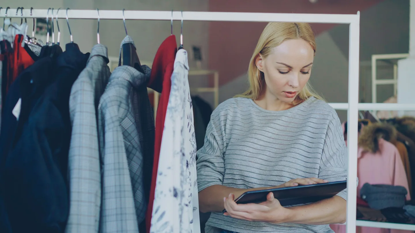 Employée utilisant une tablette parmi des vêtements en magasin