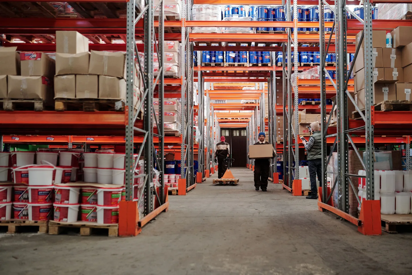 Allée d’entrepôt avec rayonnages, cartons et personnel au travail