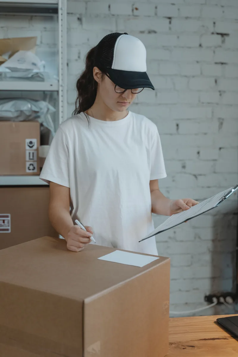 Femme vérifiant des documents parmi des cartons d’expédition