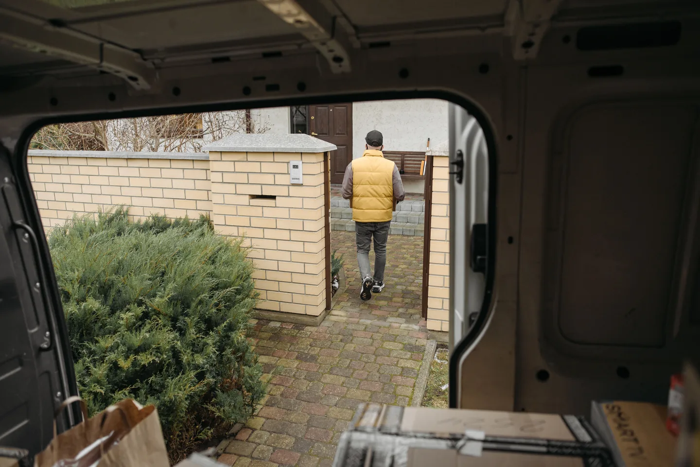 Livreur se dirigeant avec un colis depuis la camionnette vers une maison