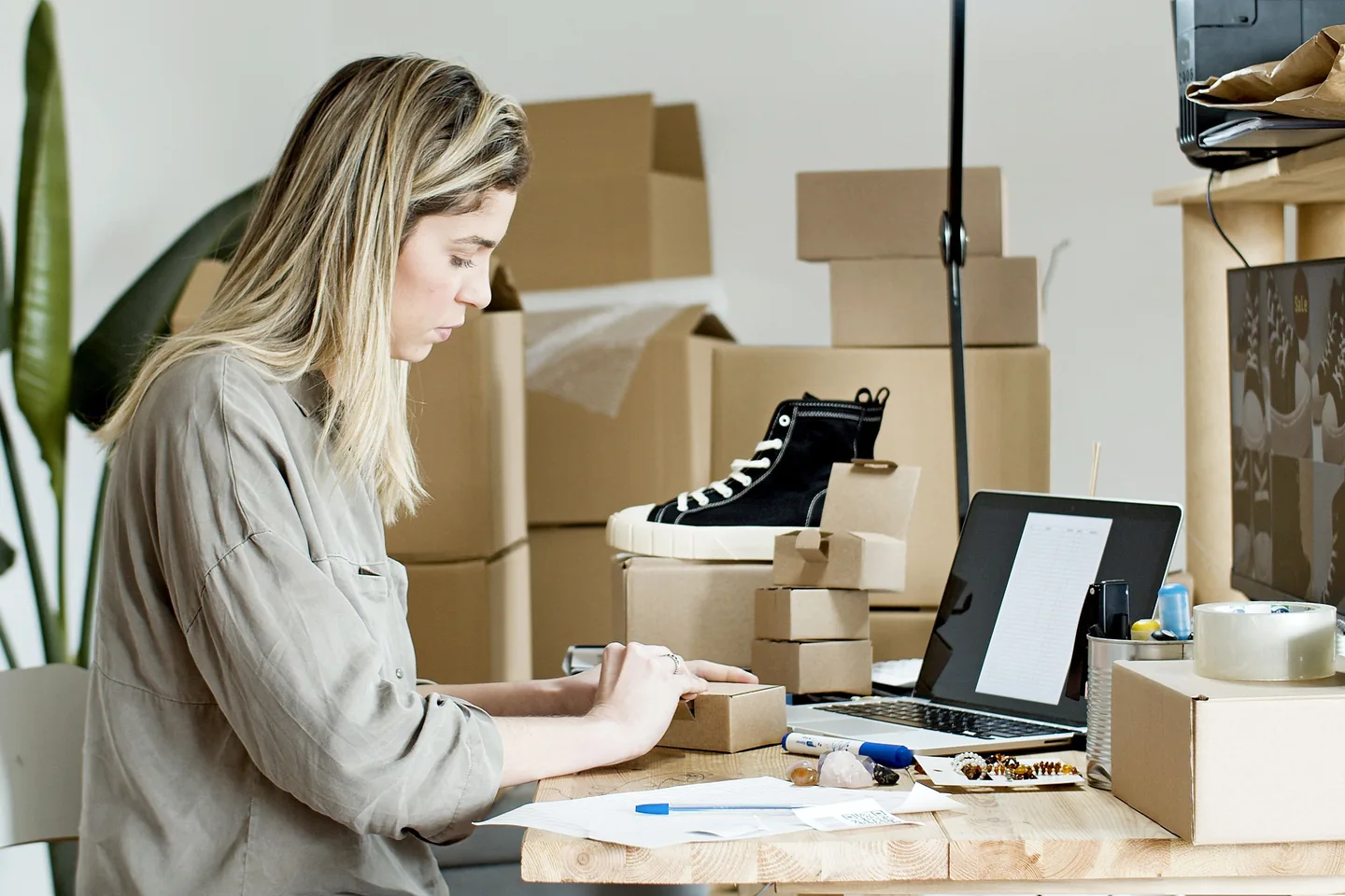 Femme préparant une commande parmi des cartons et un ordinateur portable