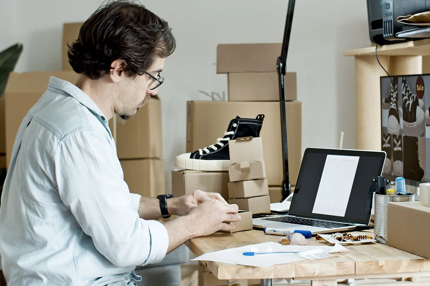Homme emballant une commande sur une table avec un ordinateur portable