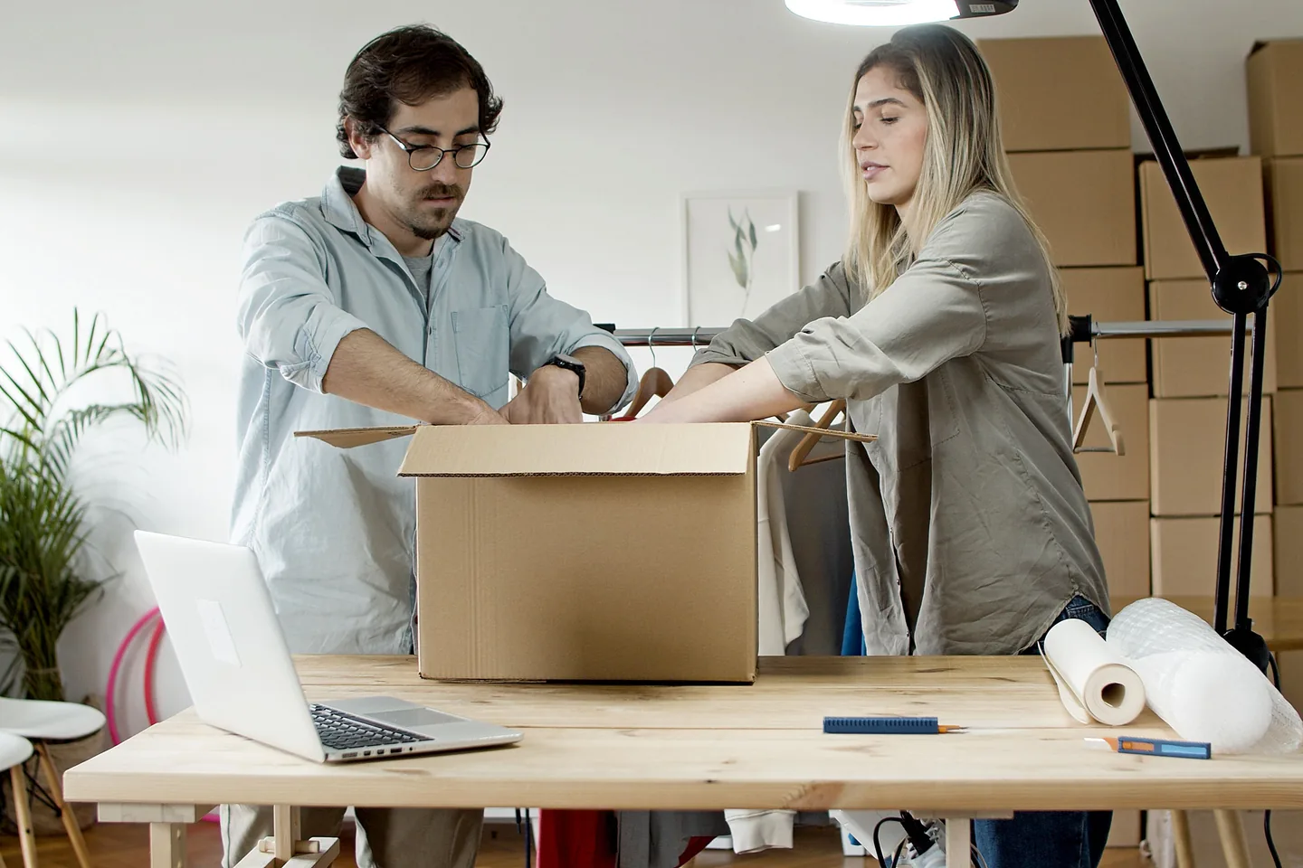 Deux personnes emballent des commandes sur une table avec un ordinateur portable